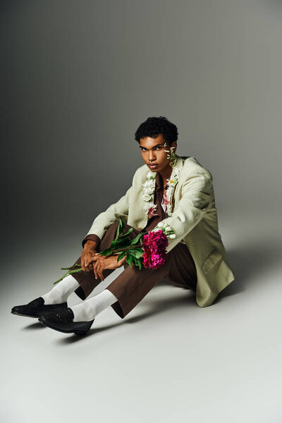 A young African American man sits gracefully with flowers adorning his neck and face.