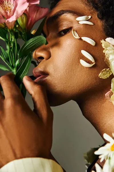 stock image A young African American man poses with flowers adorning his face and neck against a grey background.