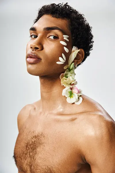 stock image A young, muscular African American man poses against a grey background, his face and body adorned with delicate white flowers.