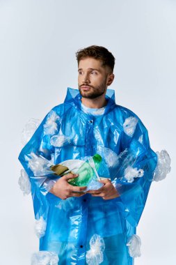 Man in blue poncho with plastic items against white backdrop. clipart