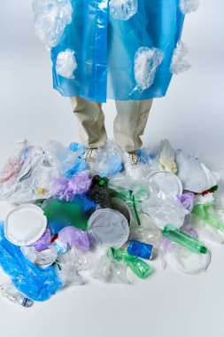 Plastik bir atık yığınının üzerinde duran bir adam, plastik bir panço giyiyor..