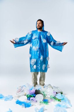 Mavi yağmurluklu adam plastik yığının üzerinde duruyor, kolları açık..
