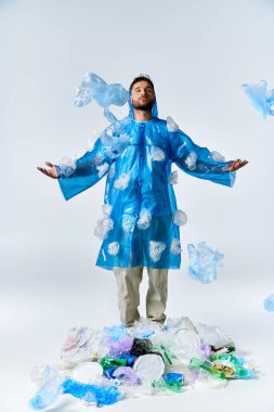 Plastik bir yağmurluğun içinde, etrafı plastik enkazlarla çevrili bir adam var..