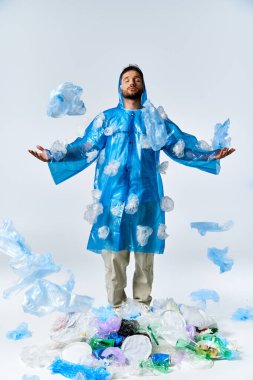 Bir adam plastiğin ortasında duruyor, mavi yağmurluğu plastik parçalarıyla süslenmiş..