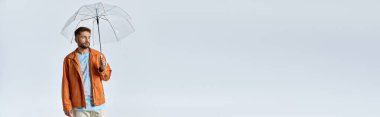 Parlak turuncu ceketli bir adam beyaz bir arka plana karşı temiz bir şemsiye tutuyor..