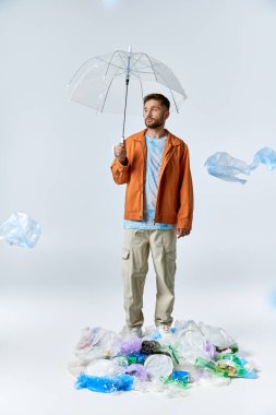 A man stands on a mound of plastic waste, holding a clear umbrella. clipart