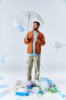 Plastik bir yığının üzerinde elinde şemsiyeyle duran bir adam etrafını naylon poşetlerle çeviriyor..
