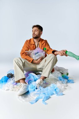 Plastik atıklarla çevrili bir adam, modern tüketim üzerine sessiz bir yorum..