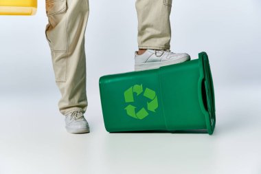 Bir adamın ayağı yeşil bir geri dönüşüm kutusunun üzerinde duruyor, sürdürülebilirliğin önemini vurguluyor..