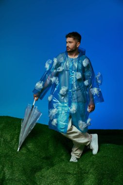 Plastik yağmurluk ve şemsiyeli adam çimlerin üzerinde duruyor, plastik torbalarla..