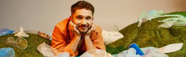 Gülümseyen bir adam, atılmış plastik poşetler ve diğer eşyalarla çevrili plastik bir denizin ortasında dinlenir..