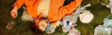 Çimenli yüzeyde atılmış plastik parçalarla çevrili bir adam..