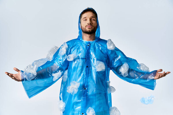 Man stands wearing blue plastic poncho and bags against plain background.