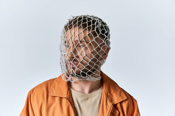 A man in an orange jacket stares into the distance, his face covered by a net.