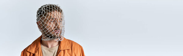 A man stands against a white backdrop, his head covered in a plastic net, his expression somber.