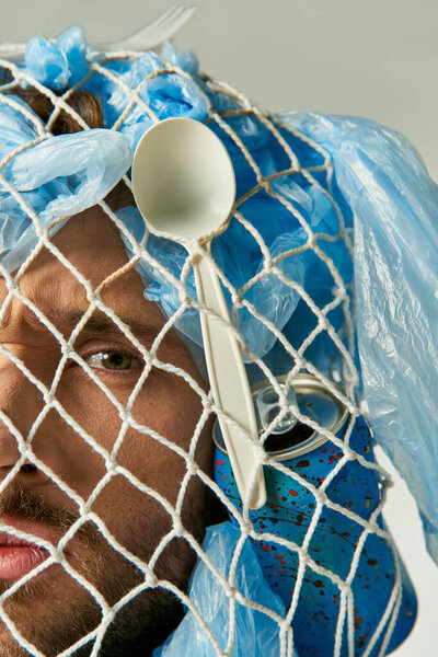 A man's face is partially obscured by a net of plastic bags and other plastic waste.