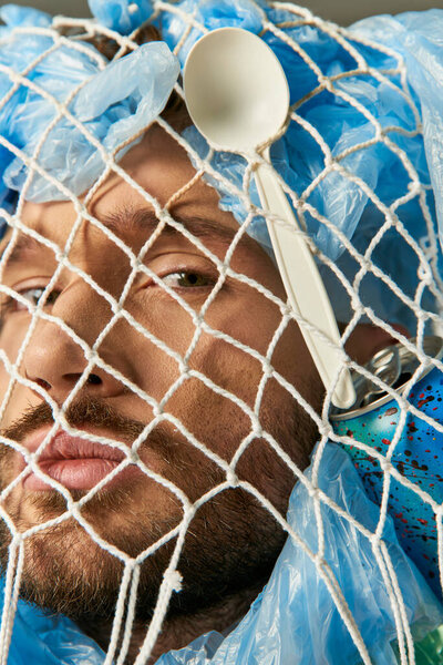A man's face is partially obscured by a net of plastic bags and a plastic spoon.
