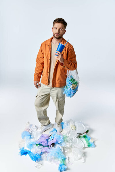 Man on plastic mountain with blue cup and bag of plastic.