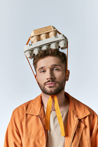 Молодой человек носит коробку с яйцами, как шляпу, с оранжевыми ремнями, свисающими вниз.