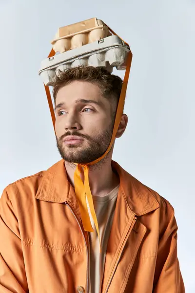 stock image A man with a beard and an orange jacket wears an egg carton crown.