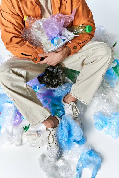 Мужчина сидит среди кучи пластиковых пакетов и бутылок, держа больше на коленях.