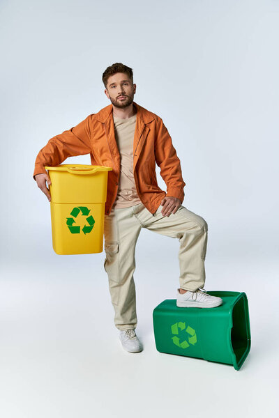 Человек уверенно стоит, держа желтый мусорный бак, с зеленым мусорным баком под ногой.