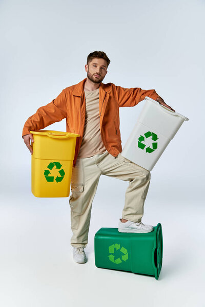 A man stands on a recycling bin, holding two more, surrounded by a white backdrop.