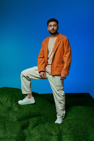 A man in an orange jacket steps on a grassy hill, surrounded by plastic objects.