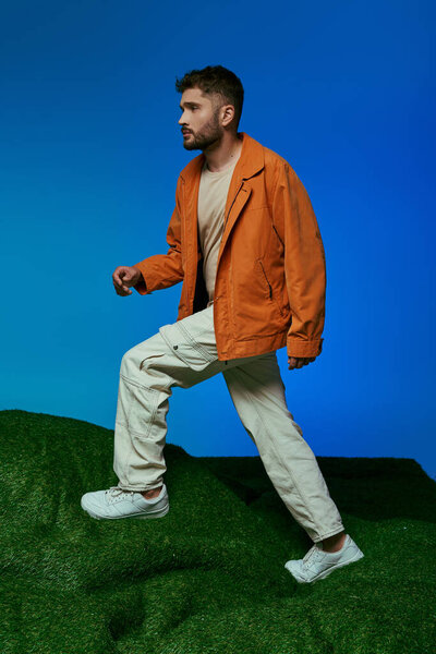 A man in an orange jacket walks on a green hill.