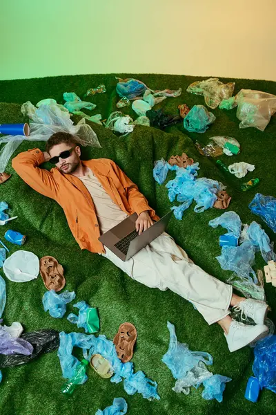 stock image A man reclines on a patch of artificial grass, surrounded by a sea of plastic waste.