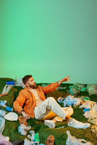 A man sits surrounded by plastic waste, reaching out with a hopeful expression.