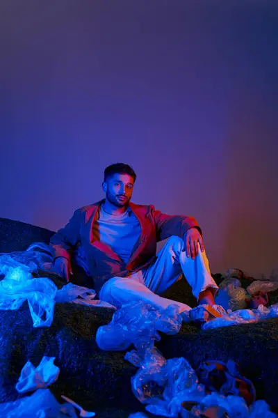 Stock image A man in studio surrounded by plastic, lit with blue and red lights.