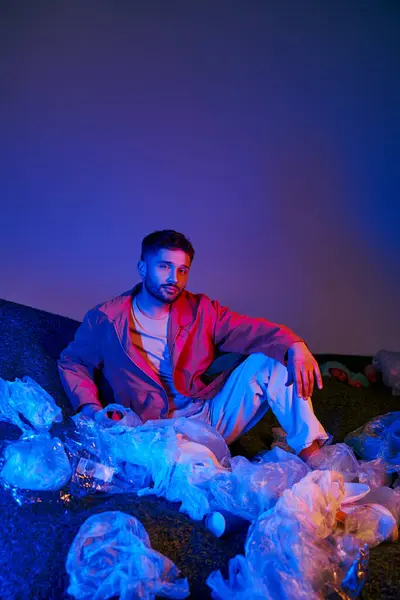 stock image A man sits amidst a sea of plastic, bathed in blue and red light.