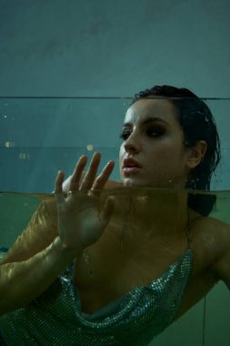 A young woman with wet hair, dressed in a shimmering outfit, floats in an underwater environment. clipart