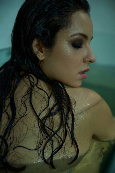 A young woman with wet, dark hair gazes downward, her skin glowing in the underwater light.
