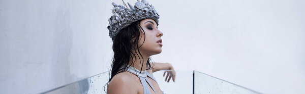 Молодая женщина с мокрыми волосами и короной из раковин мечтательно смотрит из аквариума.