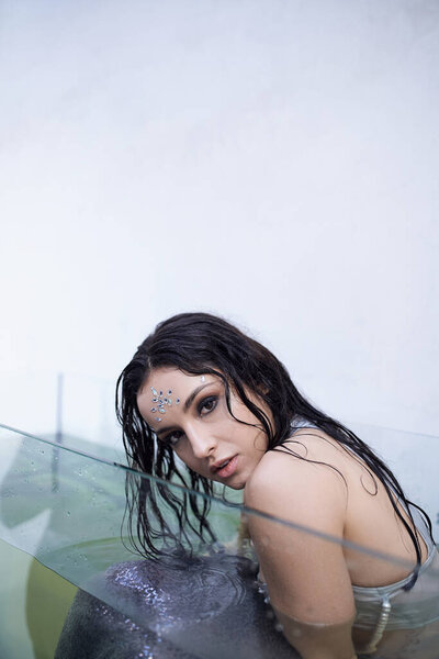 A mermaid with dark hair gazes intensely from beneath the water's surface in an aquarium.