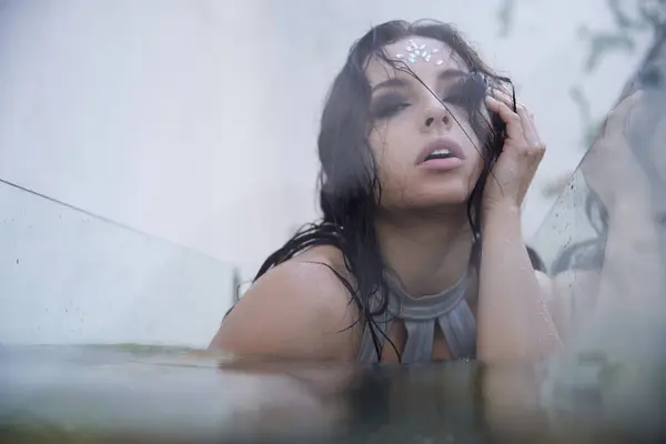 stock image A young woman with dark hair emerges from the water, resembling a mermaid in a misty aquarium.