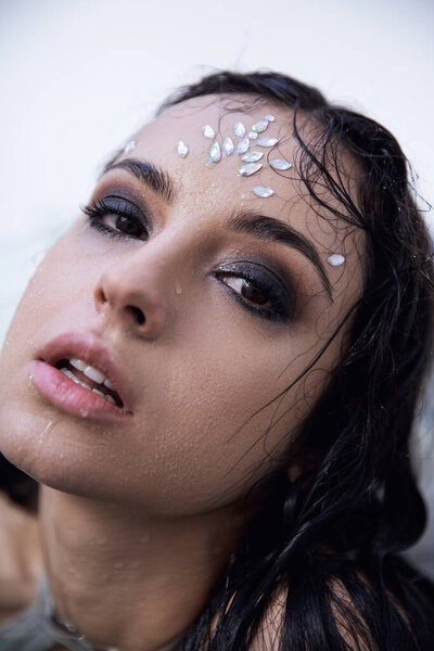 A young woman with wet hair and sparkling makeup looks up from an aquarium, hinting at a world of dreams and fantasy.