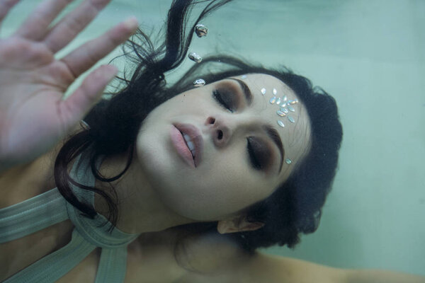 A young woman with long, dark hair floats gracefully in an aquarium, her eyes closed as if lost in a dream.