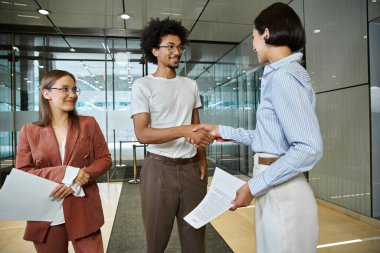 Three colleagues chat and shake hands in an office lobby. clipart