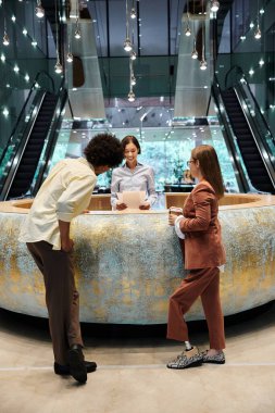 Three colleagues converse in a modern office lobby, with one woman wearing a prosthetic leg. clipart