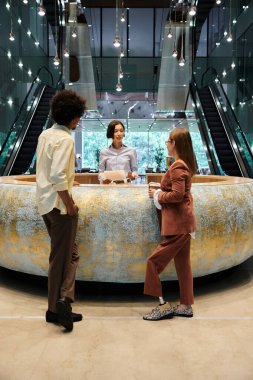 Three colleagues stand in an office lobby, engaged in conversation near a large, curved reception desk. clipart