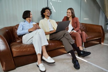 Three colleagues, including a woman with a prosthetic leg, share a laugh while sitting on a leather sofa in a modern office lobby. clipart