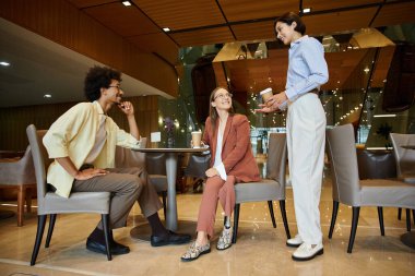 Three diverse colleagues, including a woman with a prosthetic leg, enjoy coffee and conversation in a modern office setting. clipart