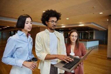 Çeşitli bir grup meslektaşım modern ofis ortamında bir dizüstü bilgisayarla sohbet edip çalışıyor..