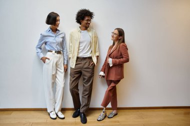 Protez bacaklı bir kadın da dahil olmak üzere üç meslektaş, beyaz bir duvara yaslanıp modern bir ofiste sohbet ediyorlar..