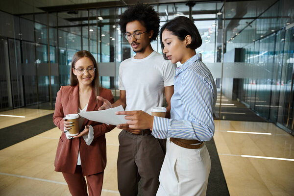 Трое коллег, включая женщину с протезной ногой, стоят в холле офиса и обсуждают бумажную работу..