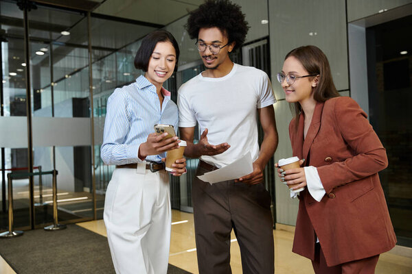 Three colleagues, engage in a friendly conversation in a modern office lobby.