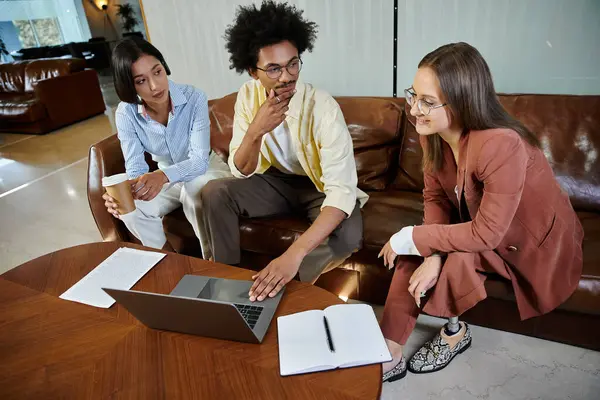 stock image Three colleagues gather in a modern office lobby, discussing ideas while using a laptop and a notebook.